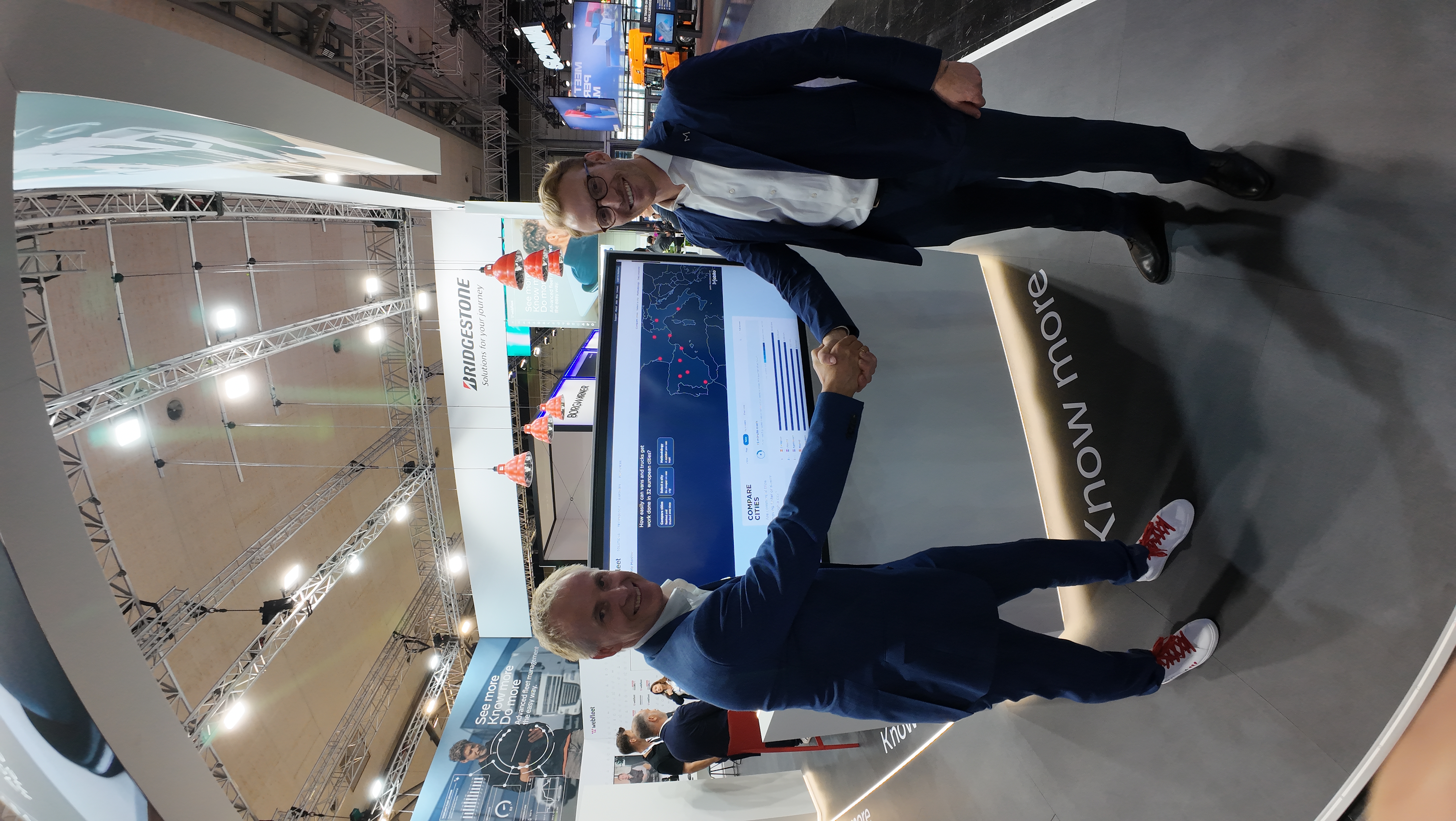 Representatives of Mobito and Webfleet shaking hands in front of the Commercial Trip Monitor at IAA Transportation 2026